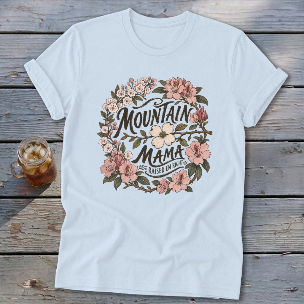 Light blue t-shirt with "Mountain Mama Raised Em Right" text within a floral wreath.