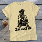 Yellow t-shirt with black graphic of a boy in overalls and cap holding a bucket, text "COAL CAMP KID".
