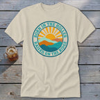 A beige t-shirt featuring a circular retro graphic with mountains, a sun, and text.