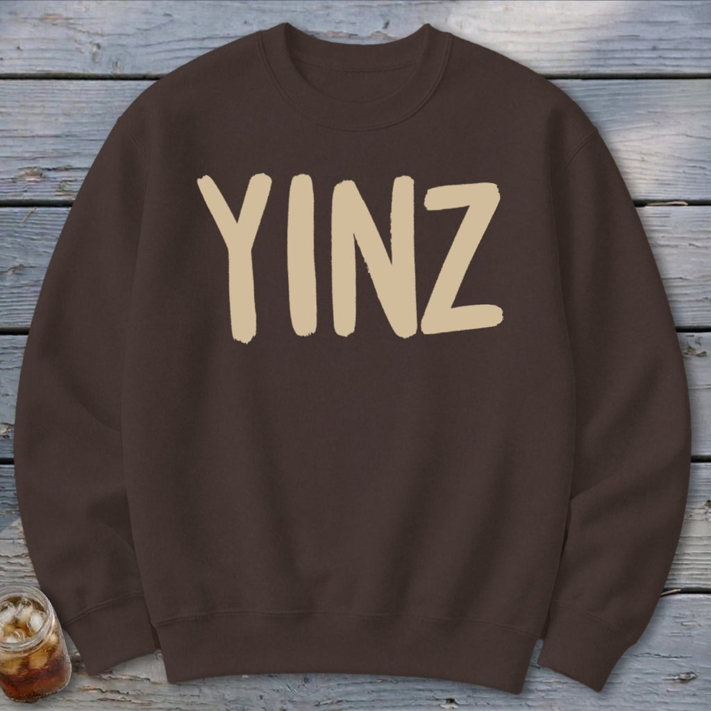 Brown crewneck sweatshirt with beige "YINZ" text, partially shown drink.