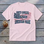 Light pink t-shirt featuring a distressed American flag and text that reads North Carolina Raised American Made.