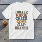 A white t-shirt featuring stacked, multi-colored retro typography spelling out HOLLER RIDGE CREEK COVE GAP BRANCH.