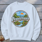 White sweatshirt with a circular Pennsylvania nature graphic featuring mountains, river, trees, deer, and sun.