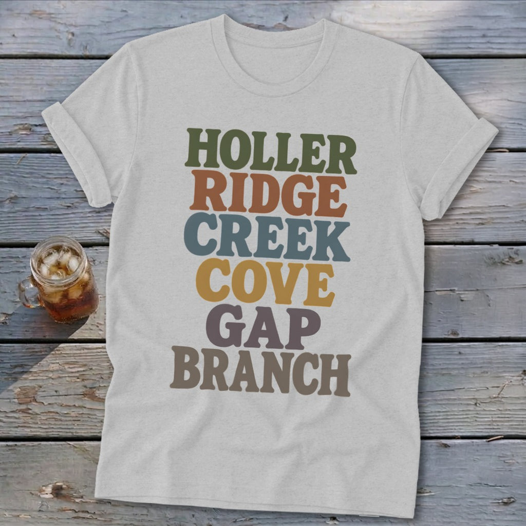 A heather gray t-shirt featuring stacked multicolored retro text resting on a rustic wooden surface.