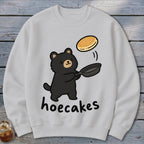 A light grey sweatshirt features a cute black bear flipping a pancake in a pan, with the text hoecakes underneath.