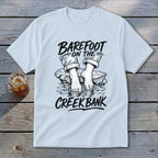White t-shirt with "Barefoot on the Creek Bank" text and illustration of feet.