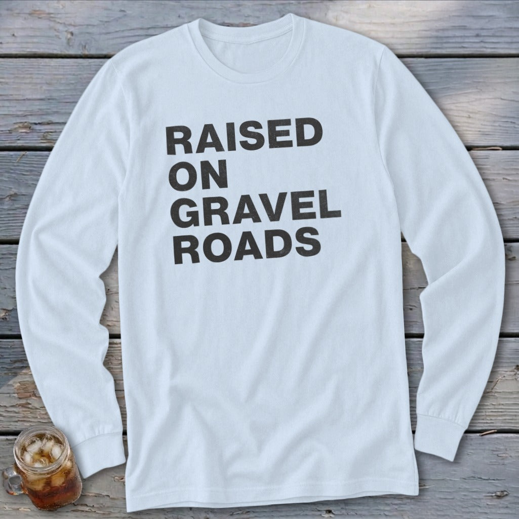 White long-sleeved shirt with "RAISED ON GRAVEL ROADS" printed in black text.