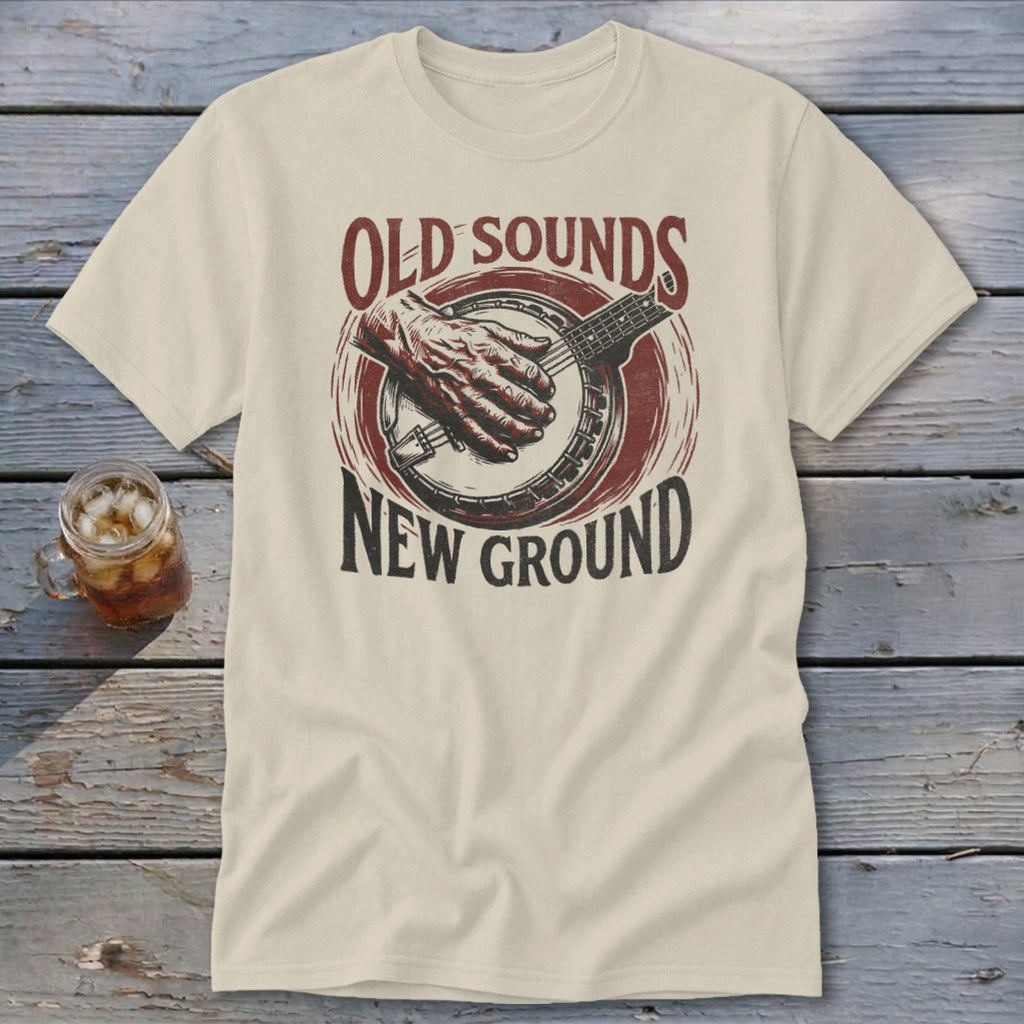 A beige t-shirt featuring a graphic of hands playing a banjo and text reading Old Sounds New Ground.