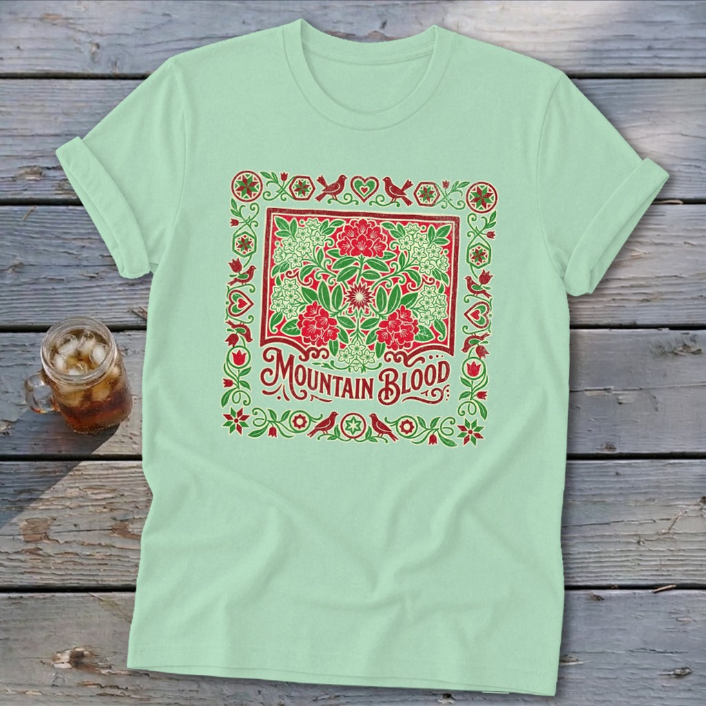 Light green t-shirt with "Mountain Blood" text and floral bird border design.