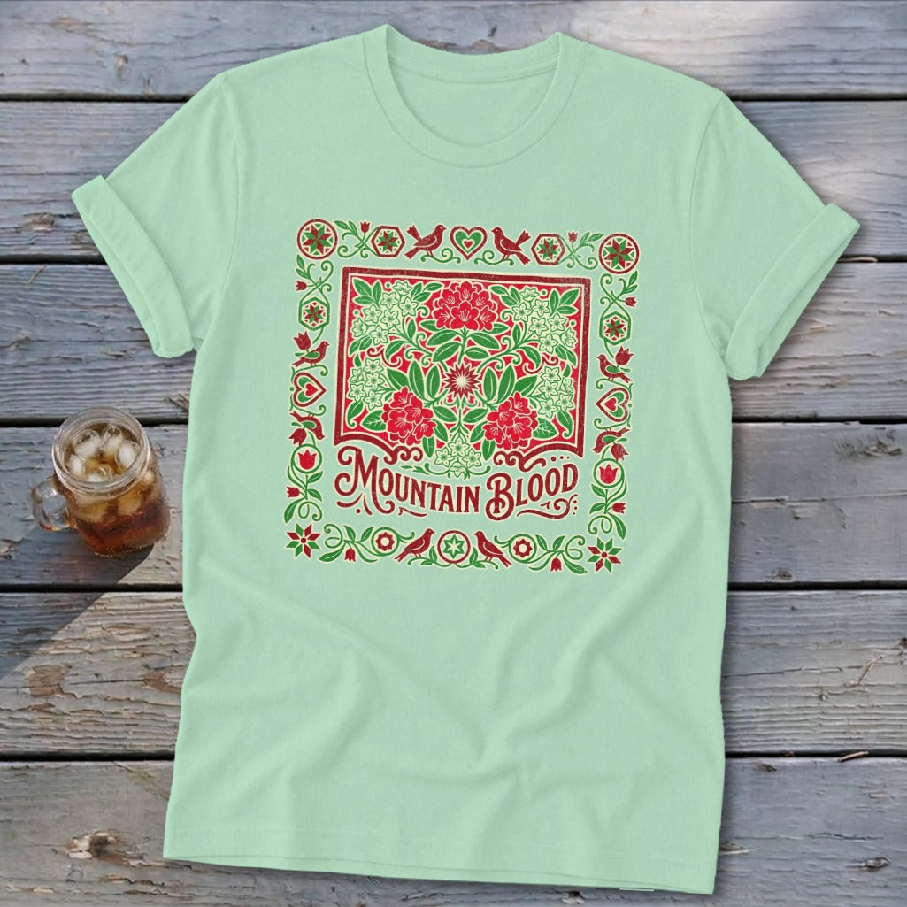 Light green t-shirt with "Mountain Blood" text and floral bird border design.