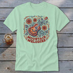 Light green crewneck t-shirt featuring a folk-art graphic of an acoustic guitar, sunflowers, and the text MOUNTAIN MELODIES.