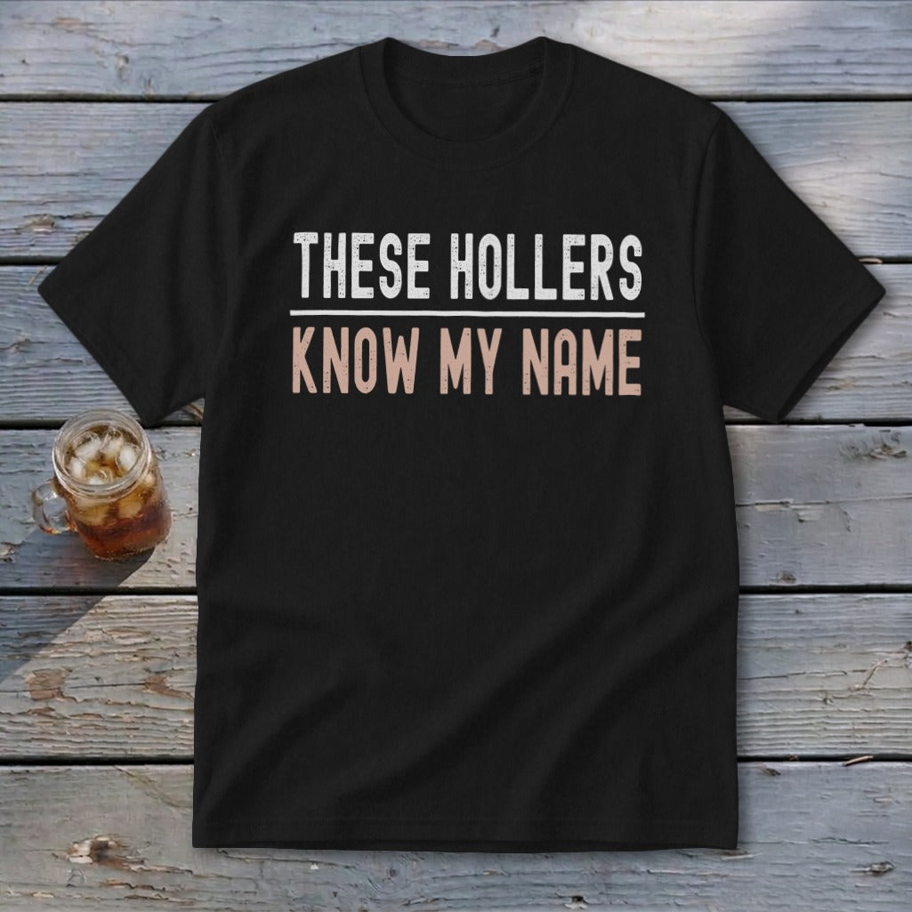 Black t-shirt with white text "THESE HOLLERS" and rose gold text "KNOW MY NAME".