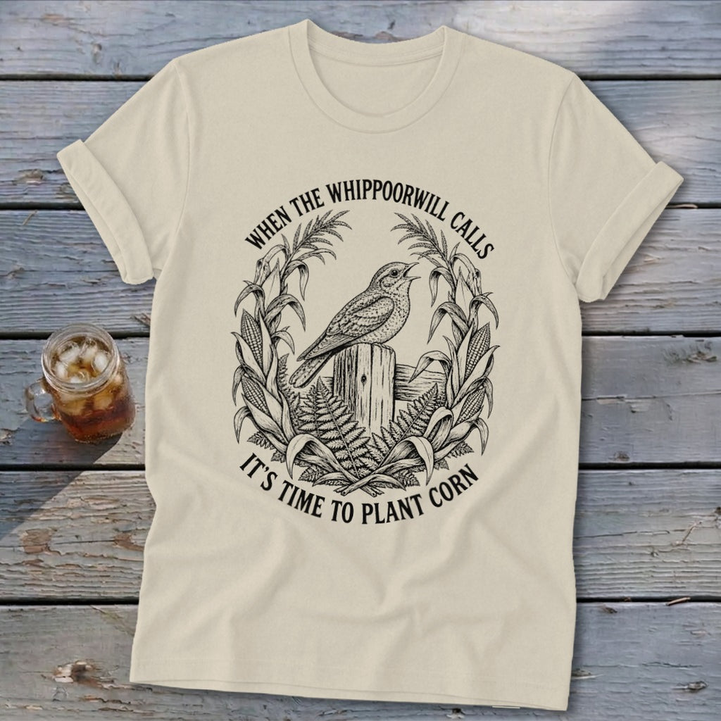 Cream crewneck t-shirt featuring a black graphic of a bird on a post surrounded by corn and the text, WHEN THE WHIPPOORWILL CALLS IT'S TIME TO PLANT CORN.