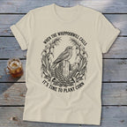 Cream crewneck t-shirt featuring a black graphic of a bird on a post surrounded by corn and the text, WHEN THE WHIPPOORWILL CALLS IT'S TIME TO PLANT CORN.