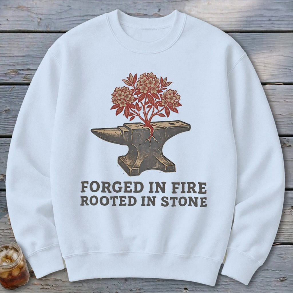 White sweatshirt with cracked anvil, blooming tree, and text "FORGED IN FIRE ROOTED IN STONE".