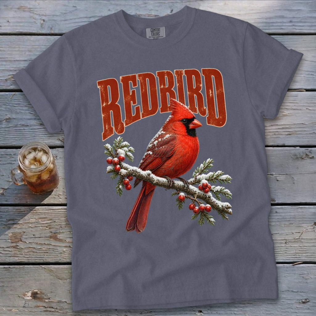 A grey crewneck t-shirt featuring a graphic of a red cardinal perched on a snowy, berry-laden branch with curved red text above reading REDBIRD.