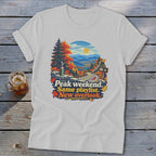 White t-shirt with mountain landscape graphic and text "Peak weekend. Same playlist. New overlook."