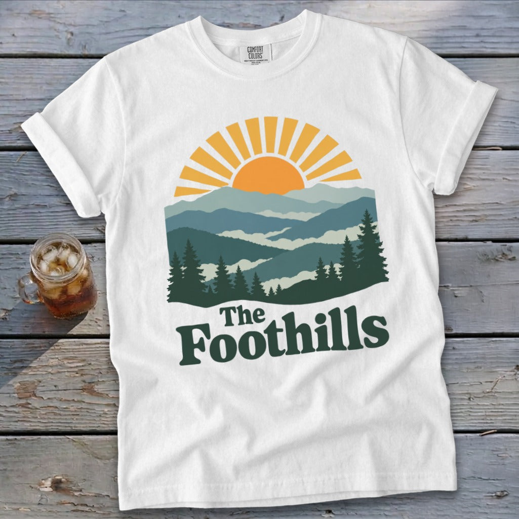 White t-shirt with sunrise over mountains and "The Foothills" text.