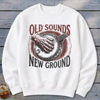 A white crewneck sweatshirt features a vintage graphic of a banjo player with text reading Old Sounds New Ground.