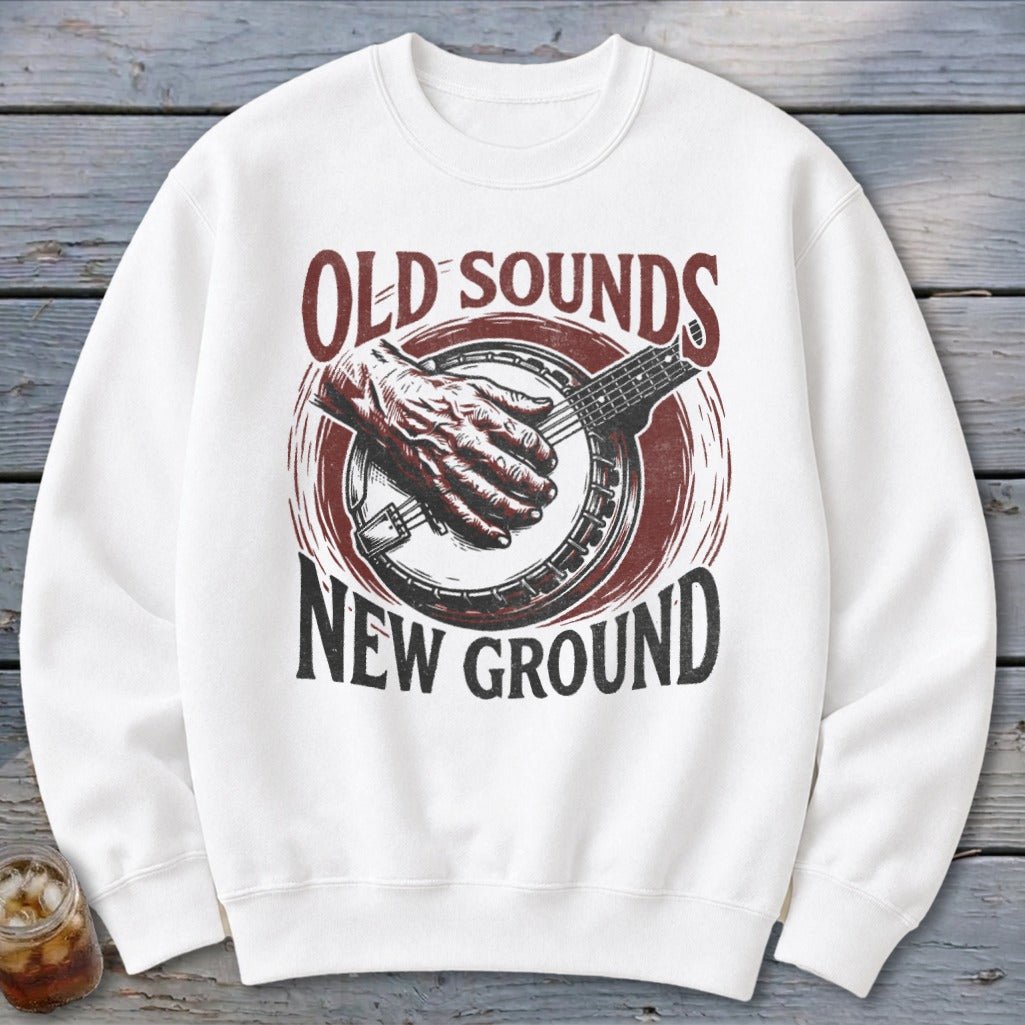 A white crewneck sweatshirt features a vintage graphic of a banjo player with text reading Old Sounds New Ground.