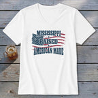 A white V-neck t-shirt with the text "MISSISSIPPI RAISED AMERICAN MADE" printed over a distressed American flag design.