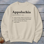 A cream-colored crewneck sweatshirt printed with black text defining Appalachia lies flat on a wooden surface.