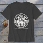 A dark gray v-neck t-shirt with white graphic text reading Certified Cornbread Judge and a round cheese illustration.