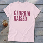Light pink t-shirt with "GEORGIA RAISED" in dark pink text.