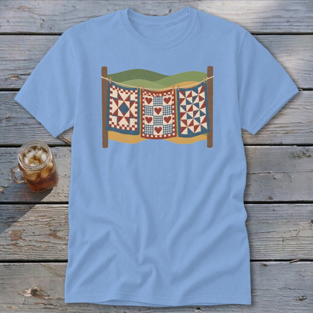 Light blue t-shirt featuring a vintage graphic of three patchwork quilts hanging on a clothesline.