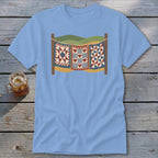 Light blue t-shirt featuring a vintage graphic of three patchwork quilts hanging on a clothesline.