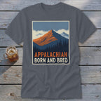 A dark grey t-shirt featuring a mountain graphic and the text "Appalachian Born and Bred" lies on a wooden surface.