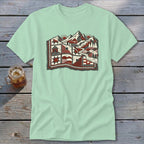 A light green t-shirt featuring a red, black, and white mountain and quilt landscape graphic.