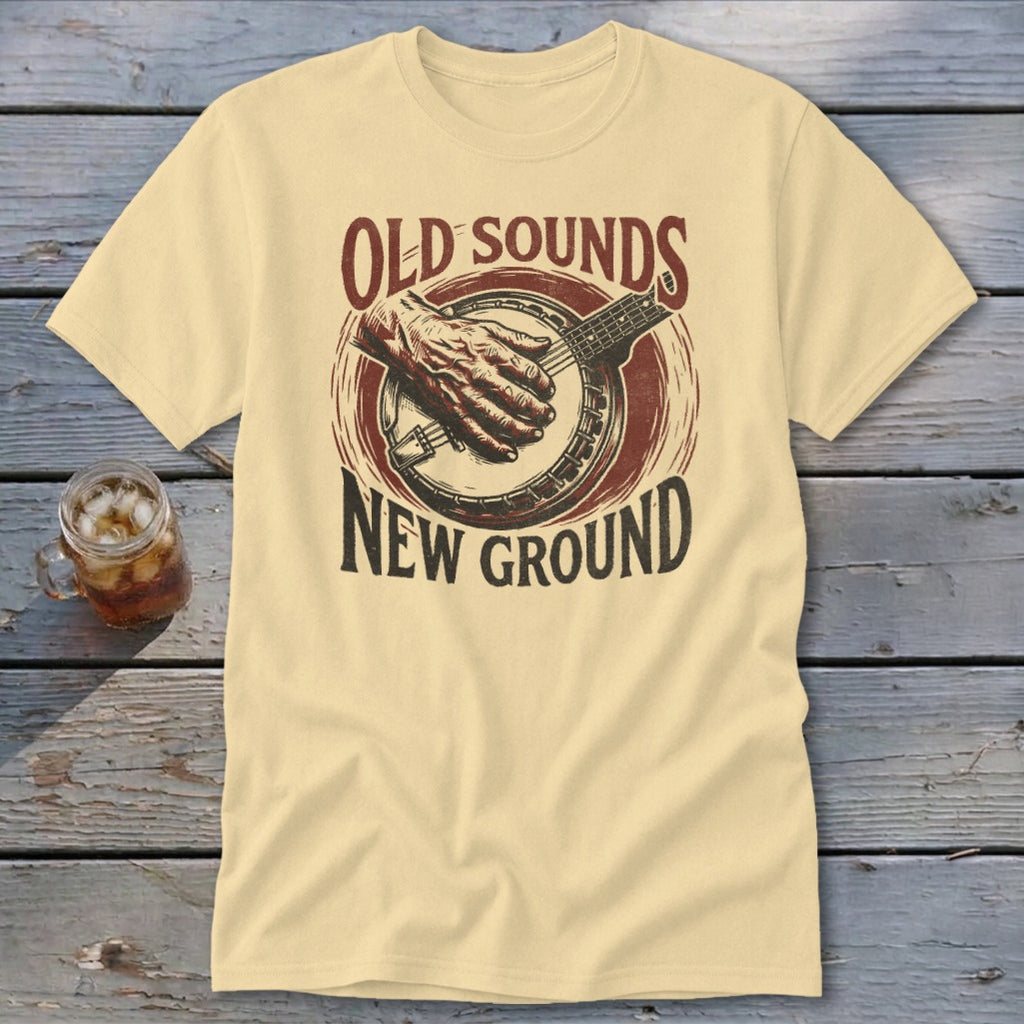 Cream t-shirt featuring a banjo graphic with a hand playing and the text Old Sounds New Ground.