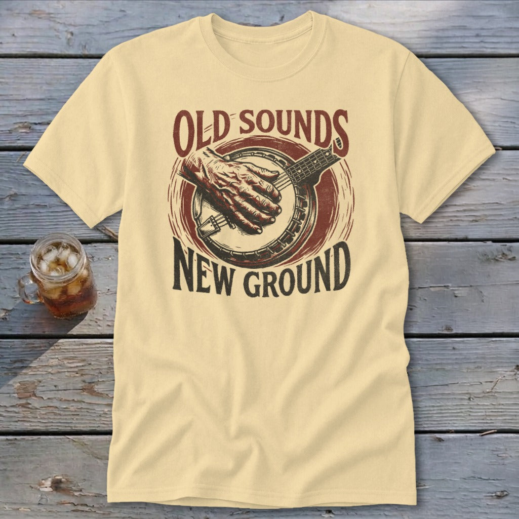 Cream t-shirt featuring a banjo graphic with a hand playing and the text Old Sounds New Ground.