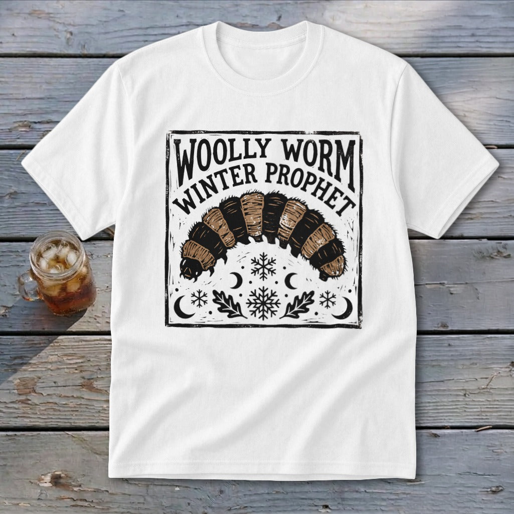 A white t-shirt featuring a black and brown block print design of a woolly worm and text reading WOLLY WORM WINTER PROPHET.