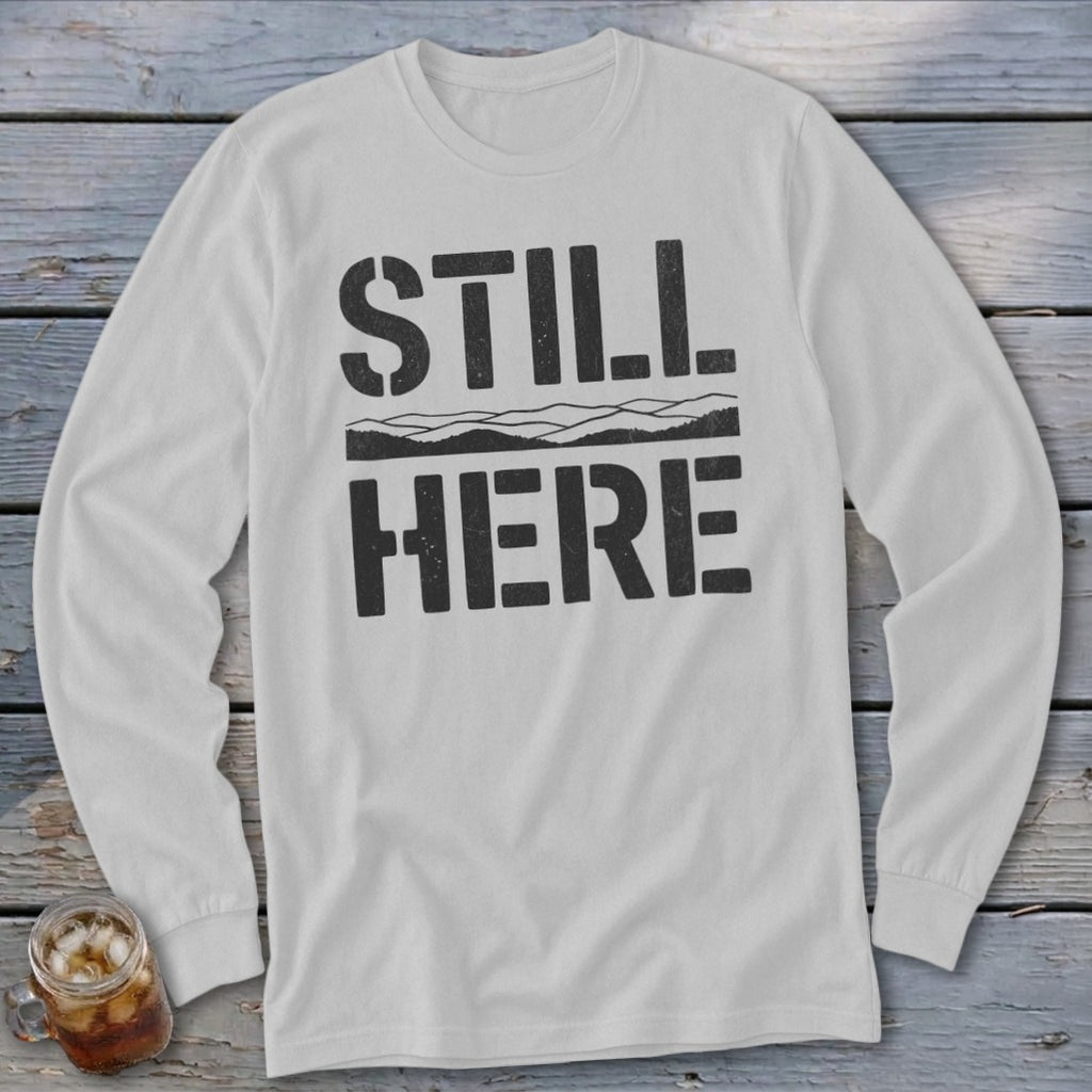 White long-sleeve shirt with black text "STILL HERE" and mountain graphic.