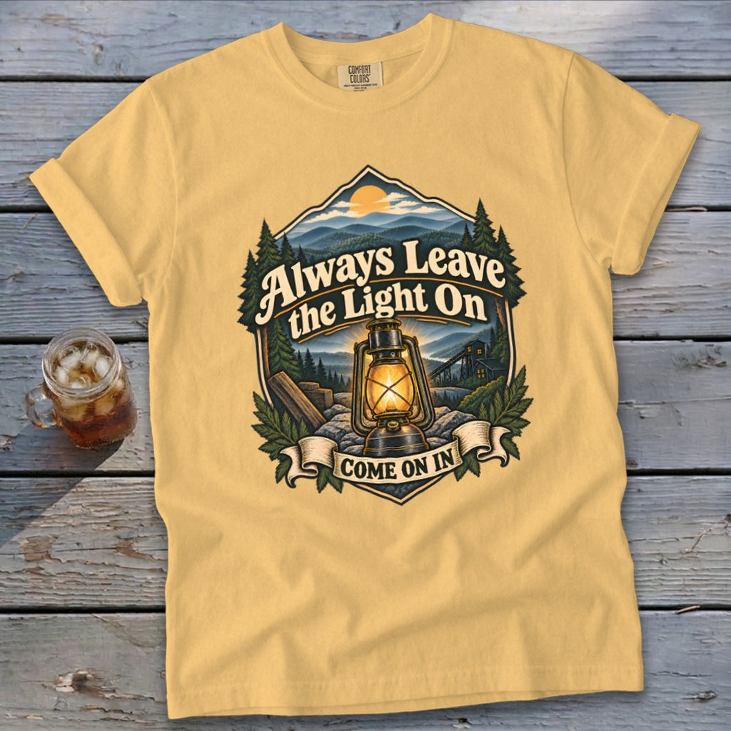 Yellow t-shirt with graphic of a lantern and mountains, reading "Always Leave the Light On Come On In".
