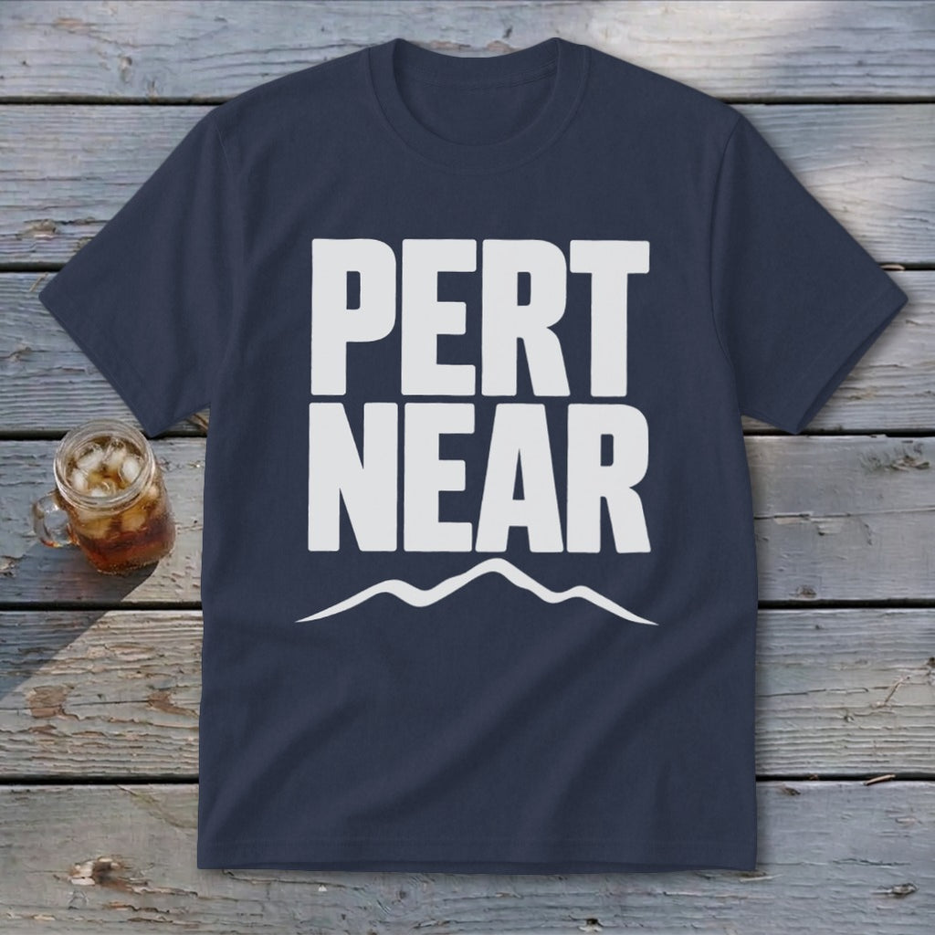 Navy blue short-sleeve t-shirt with white text reading PERT NEAR above a mountain range graphic, laid on weathered wooden planks.