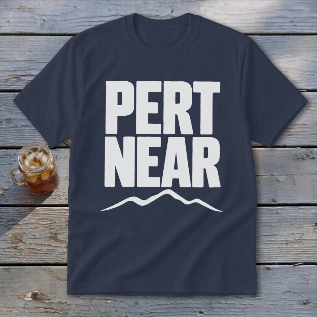 Navy blue short-sleeve t-shirt with white text reading PERT NEAR above a mountain range graphic, laid on weathered wooden planks.