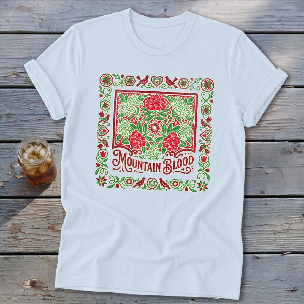 White t-shirt with red and green floral border and "Mountain Blood" text.