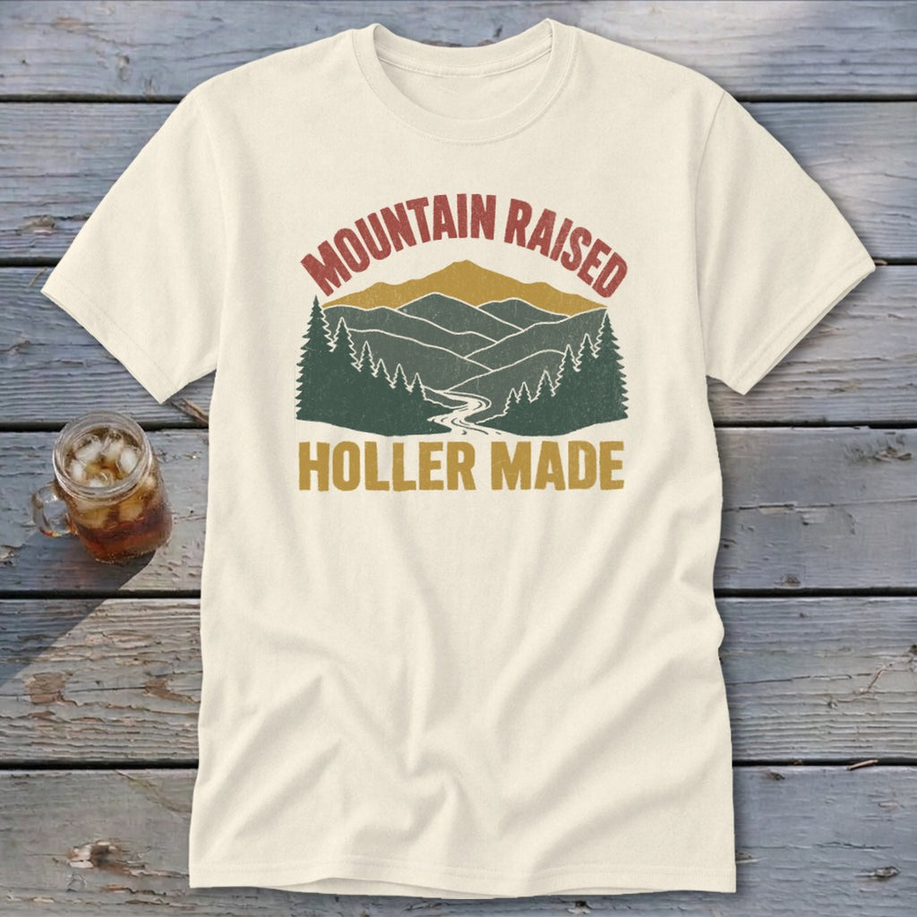 Off-white t-shirt featuring a retro graphic of mountains, trees, and the text Mountain Raised Holler Made.