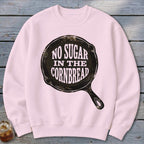 Pink sweatshirt with "NO SUGAR IN THE CORNBREAD" graphic in a cast iron skillet.