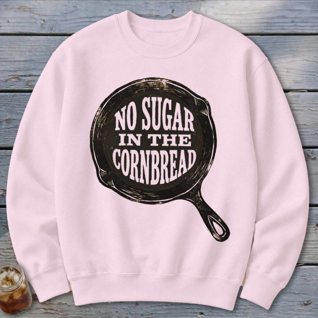 Pink sweatshirt with "NO SUGAR IN THE CORNBREAD" graphic in a cast iron skillet.
