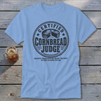 Light blue t-shirt featuring a circular graphic with text reading Certified Cornbread Judge and a cornbread illustration.