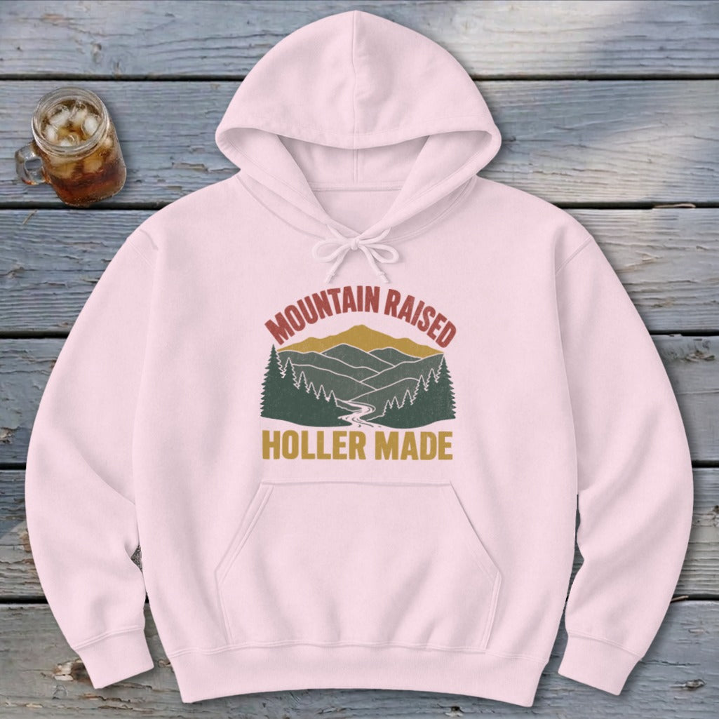 Light pink hooded sweatshirt featuring a retro graphic of mountains and the text Mountain Raised Holler Made.