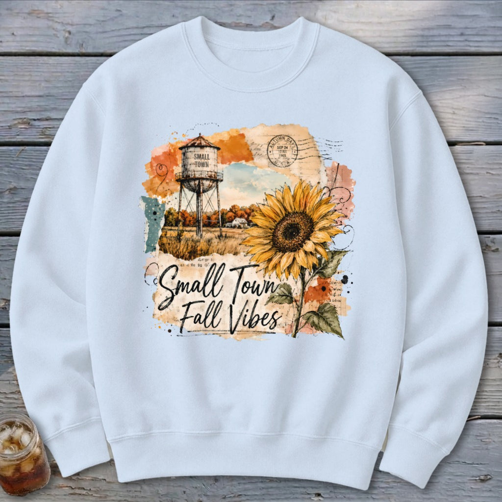 White sweatshirt with a watercolor design of a water tower, sunflower, and text "Small Town Fall Vibes".
