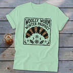 Light green t-shirt featuring a graphic of a woolly worm caterpillar, snowflakes, moons, and text reading Woolly Worm Winter Prophet.