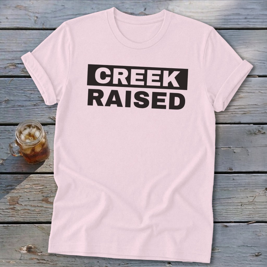 Pink t-shirt with black text "CREEK RAISED" and a drink.