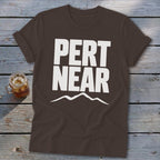 Brown crewneck t-shirt featuring bold white text that reads Pert Near above a mountain silhouette.