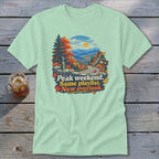 Mint t-shirt with "Peak weekend. Same playlist. New overlook." text and mountain landscape graphic.